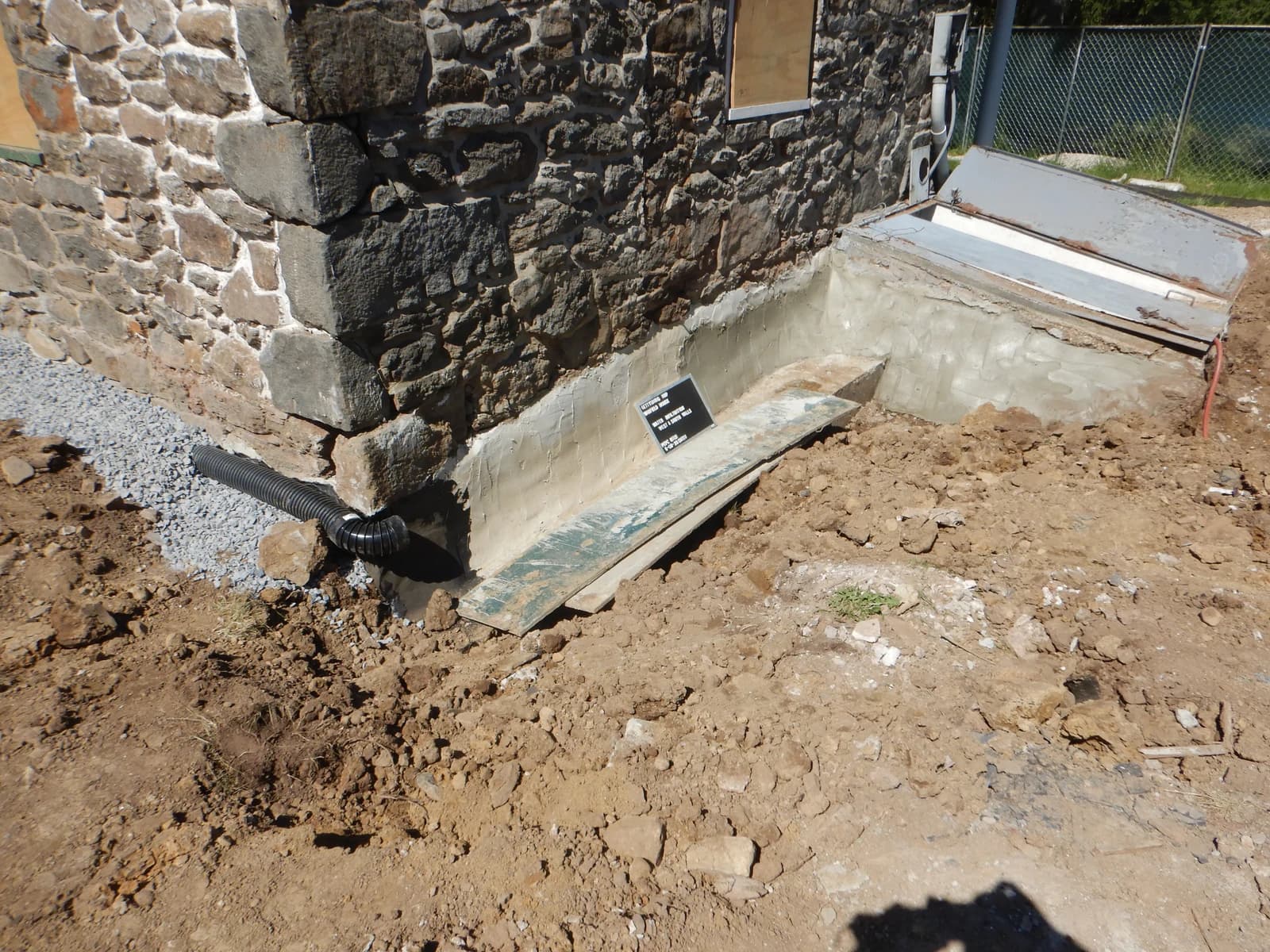 Svart korrugert drensrør lagt langs fundament og rundt hjørnet på et steinhus.
