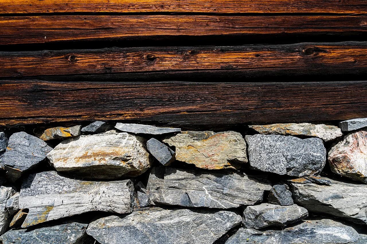Uregelmessig natursteinsfundament under en eldre laftet trevegg.