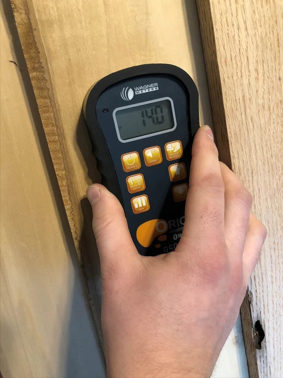 En hånd holder en fuktmåler mot en treflate.